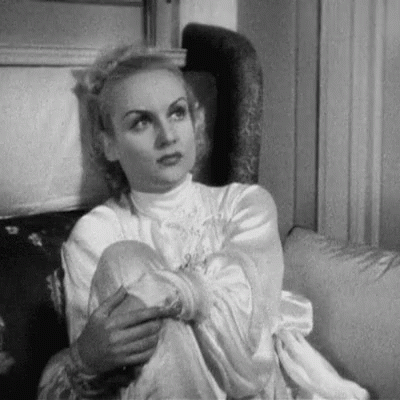 A Black And White Photo Of A Woman Sitting On A Couch With Her Legs Crossed . GIF