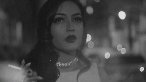 A Black And White Photo Of A Woman Smoking A Cigarette In A Dark Room . GIF
