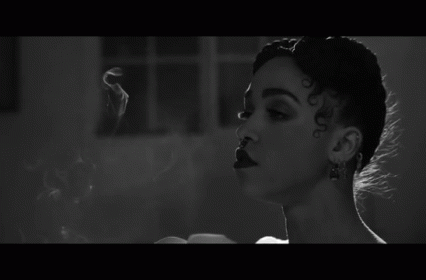 A Black And White Photo Of A Woman Smoking A Cigarette In A Room . GIF
