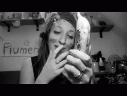 A Black And White Photo Of A Woman Smoking A Cigarette In Front Of A Fiumer Sign GIF