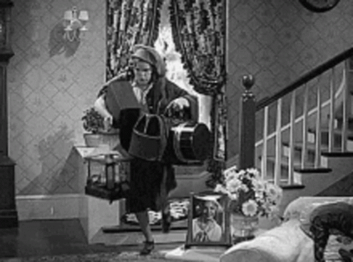 A Black And White Photo Of A Woman Standing In A Living Room Holding A Birdcage . GIF