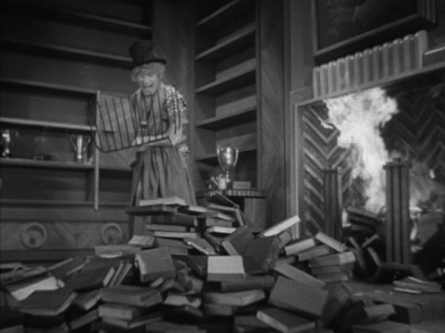 A Black And White Photo Of A Woman Standing In Front Of A Pile Of Books GIF