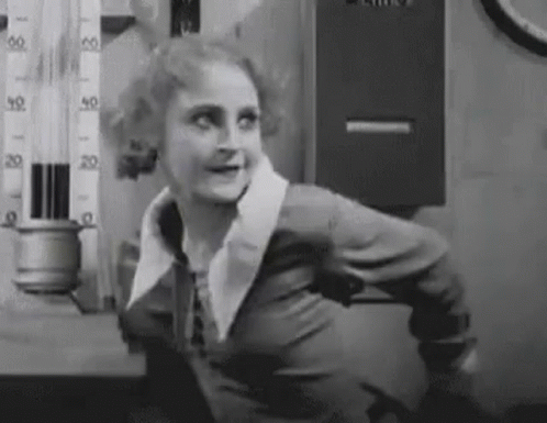 A Black And White Photo Of A Woman Standing In Front Of A Thermometer And Smiling . GIF