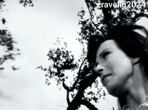 A Black And White Photo Of A Woman Standing In Front Of A Tree . GIF