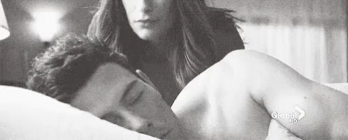 A Black And White Photo Of A Woman Standing Next To A Man Laying In Bed . GIF