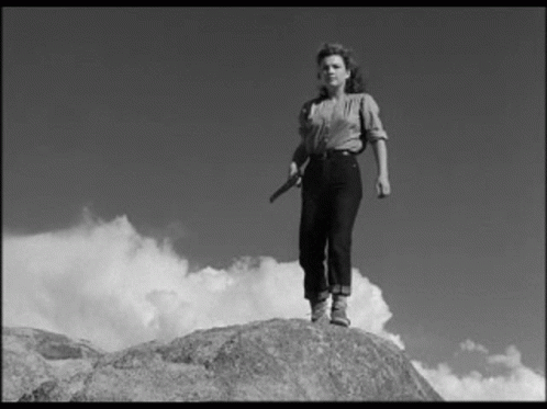 A Black And White Photo Of A Woman Standing On A Rock Holding A Knife . GIF