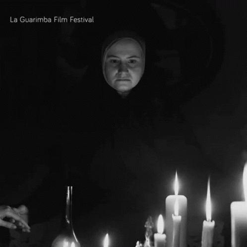 A Black And White Photo Of A Woman Surrounded By Lit Candles And The Words La Guarimba Film Festival Below Her GIF