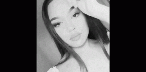 A Black And White Photo Of A Woman Taking A Selfie With Her Hand On Her Face . GIF