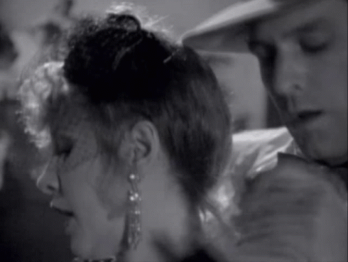 A Black And White Photo Of A Woman Wearing Earrings And A Man Wearing A Hat GIF