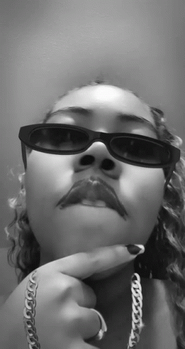 A Black And White Photo Of A Woman Wearing Sunglasses And A Silver Chain GIF