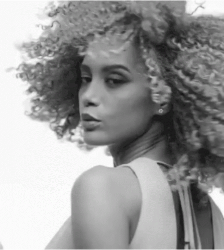A Black And White Photo Of A Woman With Curly Hair And Earrings GIF