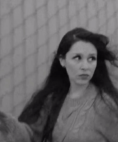a black and white photo of a woman with long hair in front of a fence .