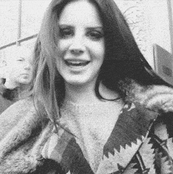 A Black And White Photo Of A Woman With Long Hair Wearing A Fur Coat And Smiling . GIF