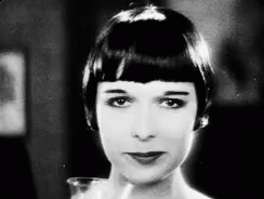A Black And White Photo Of A Woman With Short Hair Looking At The Camera . GIF