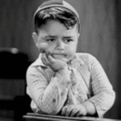 A Black And White Photo Of A Young Boy Sitting At A Desk With His Hand On His Chin . GIF