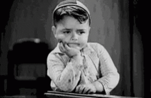 A Black And White Photo Of A Young Boy Sitting At A Desk With His Hand On His Face . GIF