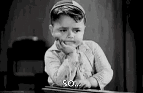 A Black And White Photo Of A Young Boy Sitting At A Desk With His Hand On His Face . GIF