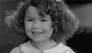 A Black And White Photo Of A Young Girl With Curly Hair Smiling . GIF