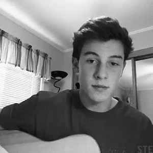 A Black And White Photo Of A Young Man Holding A Guitar In A Room . GIF