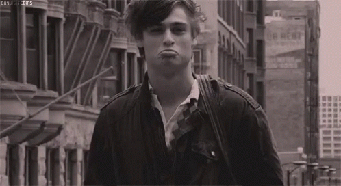 A Black And White Photo Of A Young Man Making A Funny Face While Walking Down A City Street . GIF