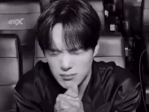 A Black And White Photo Of A Young Man Sitting In A Theater With His Eyes Closed And His Hands Folded . GIF