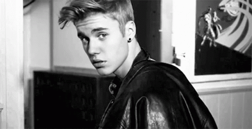 A Black And White Photo Of A Young Man Wearing A Leather Jacket And Earrings . GIF