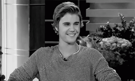 A Black And White Photo Of A Young Man Wearing A Striped Shirt Smiling . GIF