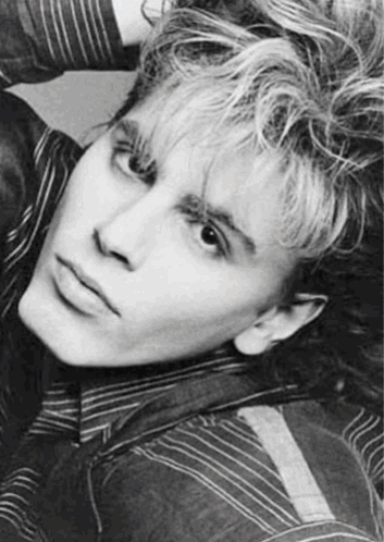 A Black And White Photo Of A Young Man With Curly Hair And A Striped Shirt . GIF