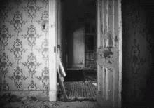 A Black And White Photo Of An Old House With A Door Open And A Staircase . GIF