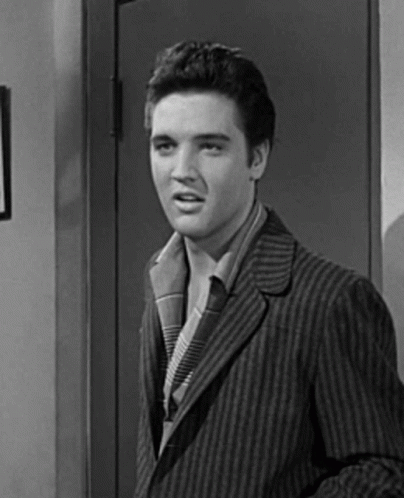 A Black And White Photo Of Elvis Presley In A Striped Suit Standing In Front Of A Door . GIF