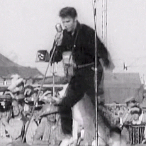 A Black And White Photo Of Elvis Presley Playing A Guitar And Singing Into A Microphone On A Stage . GIF
