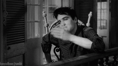 A Black And White Photo Of Elvis Presley Sitting In A Rocking Chair And Waving His Hand . GIF
