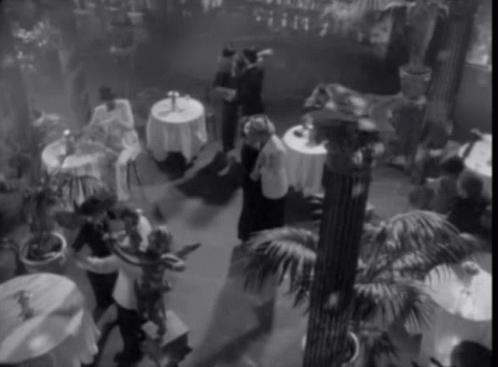 A Black And White Photo Of People Dancing In A Room With Tables GIF