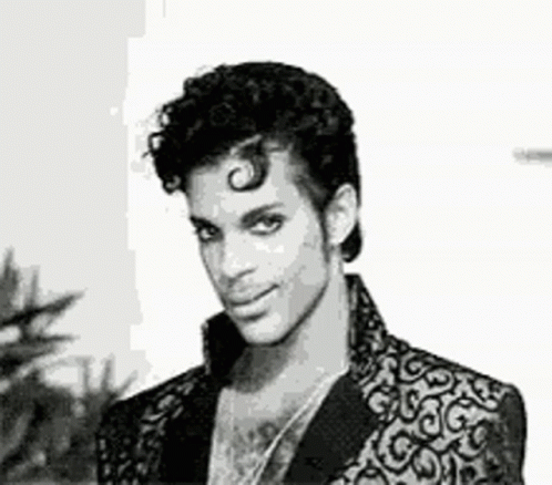 A Black And White Photo Of Prince Wearing A Suit Jacket And Necklace . GIF