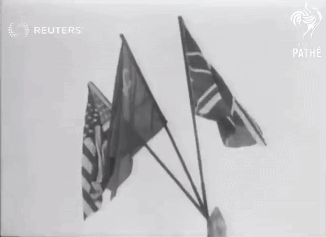 A Black And White Photo Of Three Flags With The Reuters Logo In The Background GIF
