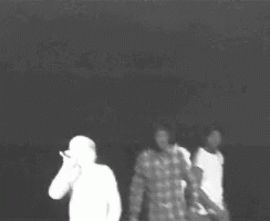 A Black And White Photo Of Three People Standing Next To Each Other In A Dark Room . GIF