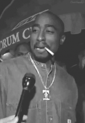 A Black And White Photo Of Tupac Shakur Smoking A Cigarette While Holding A Microphone . GIF