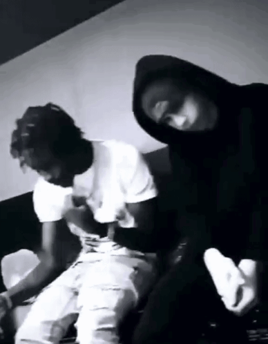 A Black And White Photo Of Two Men Sitting On A Couch . One Of The Men Is Wearing A Mask . GIF
