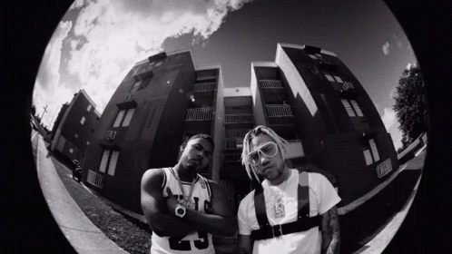 A Black And White Photo Of Two Men Standing In Front Of A Building With One Wearing A Number 9 Jersey GIF