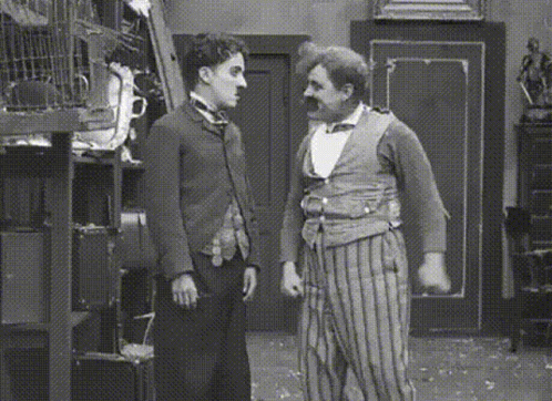 A Black And White Photo Of Two Men Standing Next To Each Other In A Room GIF