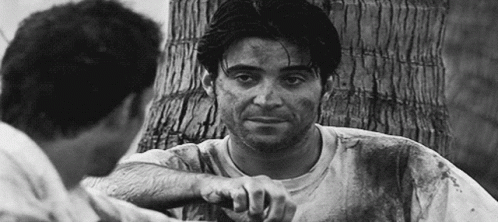 A Black And White Photo Of Two Men Talking To Each Other . One Of The Men Is Holding A Knife . GIF