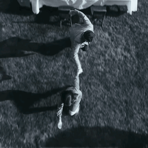 A Black And White Photo Of Two People Standing Next To Each Other On A Grassy Field GIF