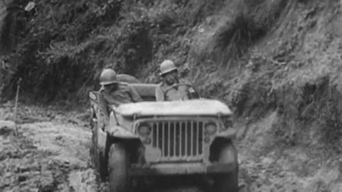 A Black And White Photo Of Two Soldiers Driving A Jeep Down A Dirt Road . GIF