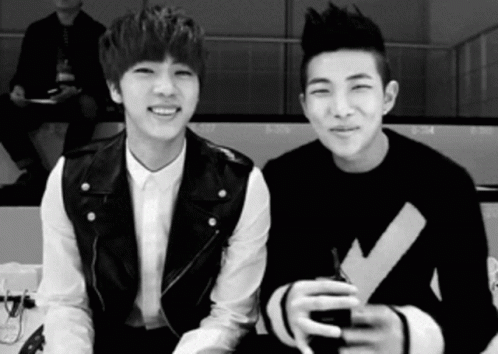 A Black And White Photo Of Two Young Men Sitting Next To Each Other And Smiling . GIF