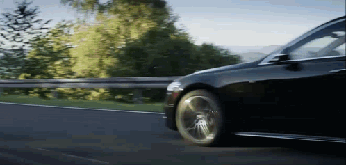 A Black Car Is Driving Down A Country Road GIF