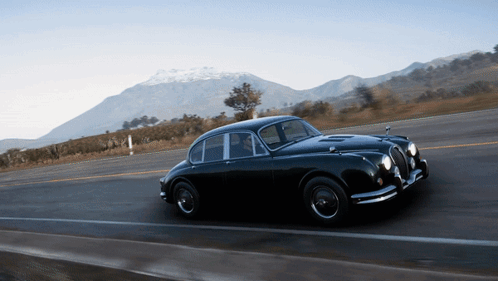 A Black Car Is Driving Down A Road In Front Of Mountains GIF
