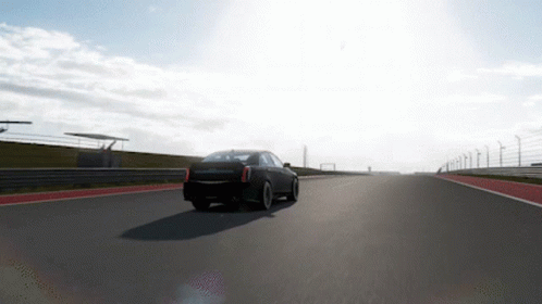 A Black Car Is Driving Down A Road With A Fence In The Background GIF