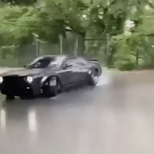 A Black Car Is Driving Down A Street With Trees In The Background . GIF