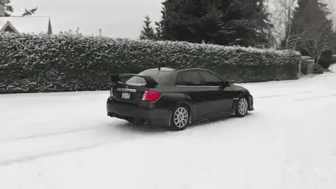 A Black Car Is Driving In The Snow On A Snowy Road . GIF