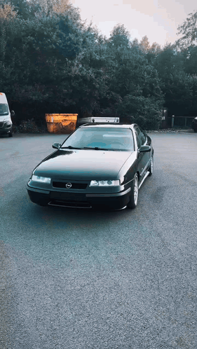 A Black Car Is Parked In A Parking Lot Next To A Yellow Dumpster GIF